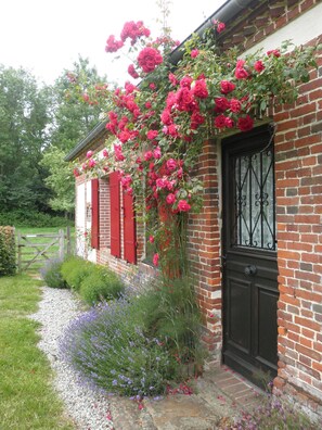 Una casa de ladrillo con contraventanas rojas, una puerta negra y un jardín con flores y un camino de grava.