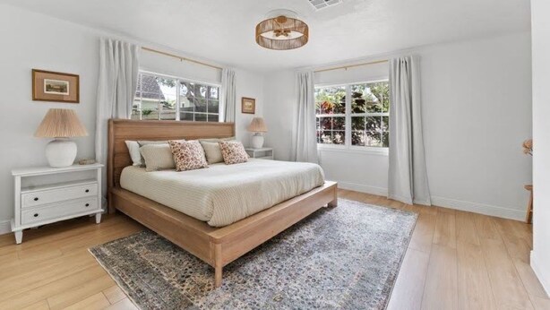 A bedroom with a wooden bed, white nightstands, a patterned rug, and large windows with curtains. - BayBreeze Cottage • Family-Friendly • Sleeps 6-8 • Near SRQ, Ringling & Beaches (Sarasota)