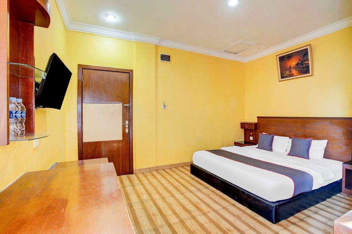 A hotel room with a bed, a desk, a television, and a painting on the wall.