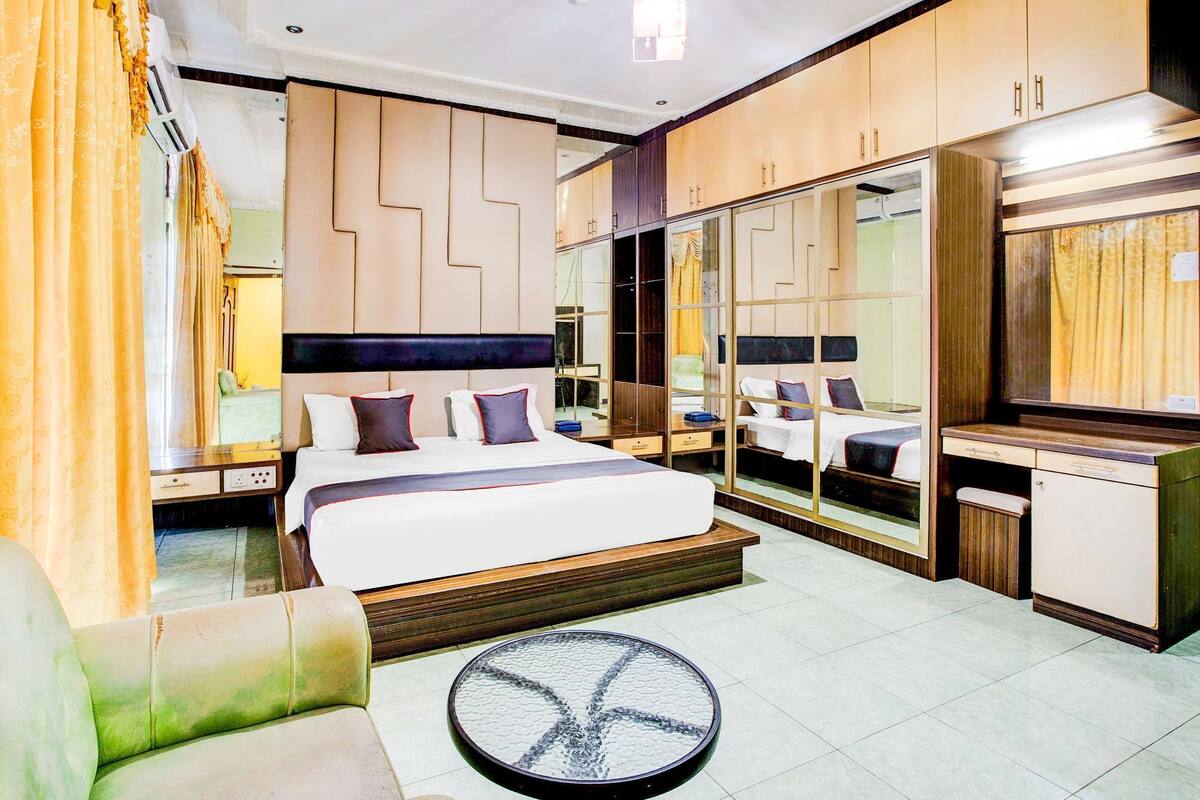 A modern hotel room with a large bed, a desk, a mirror, and a seating area.