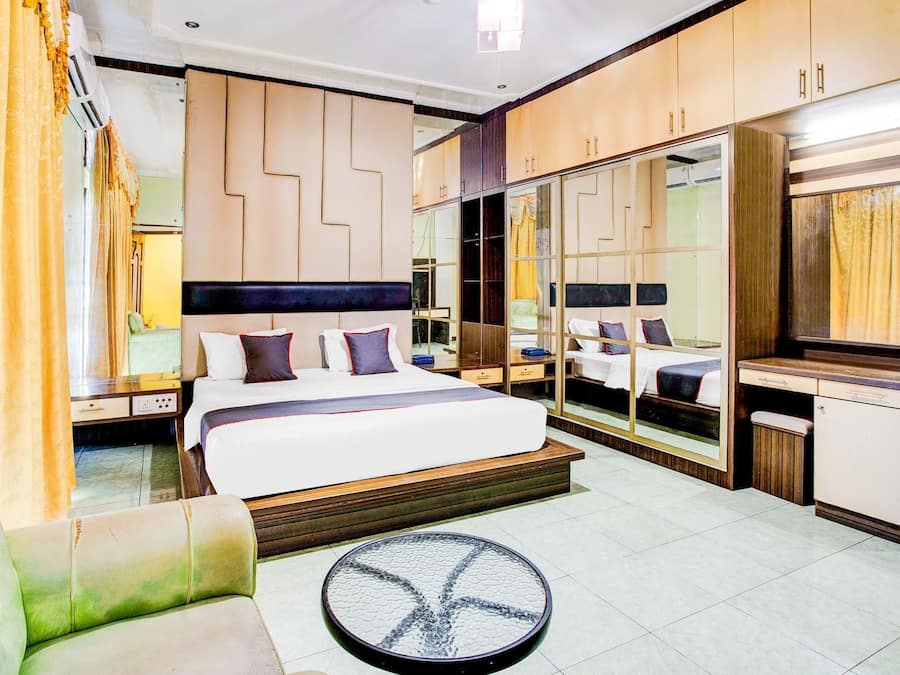 A modern hotel room with a large bed, a desk, a mirror, and a seating area.