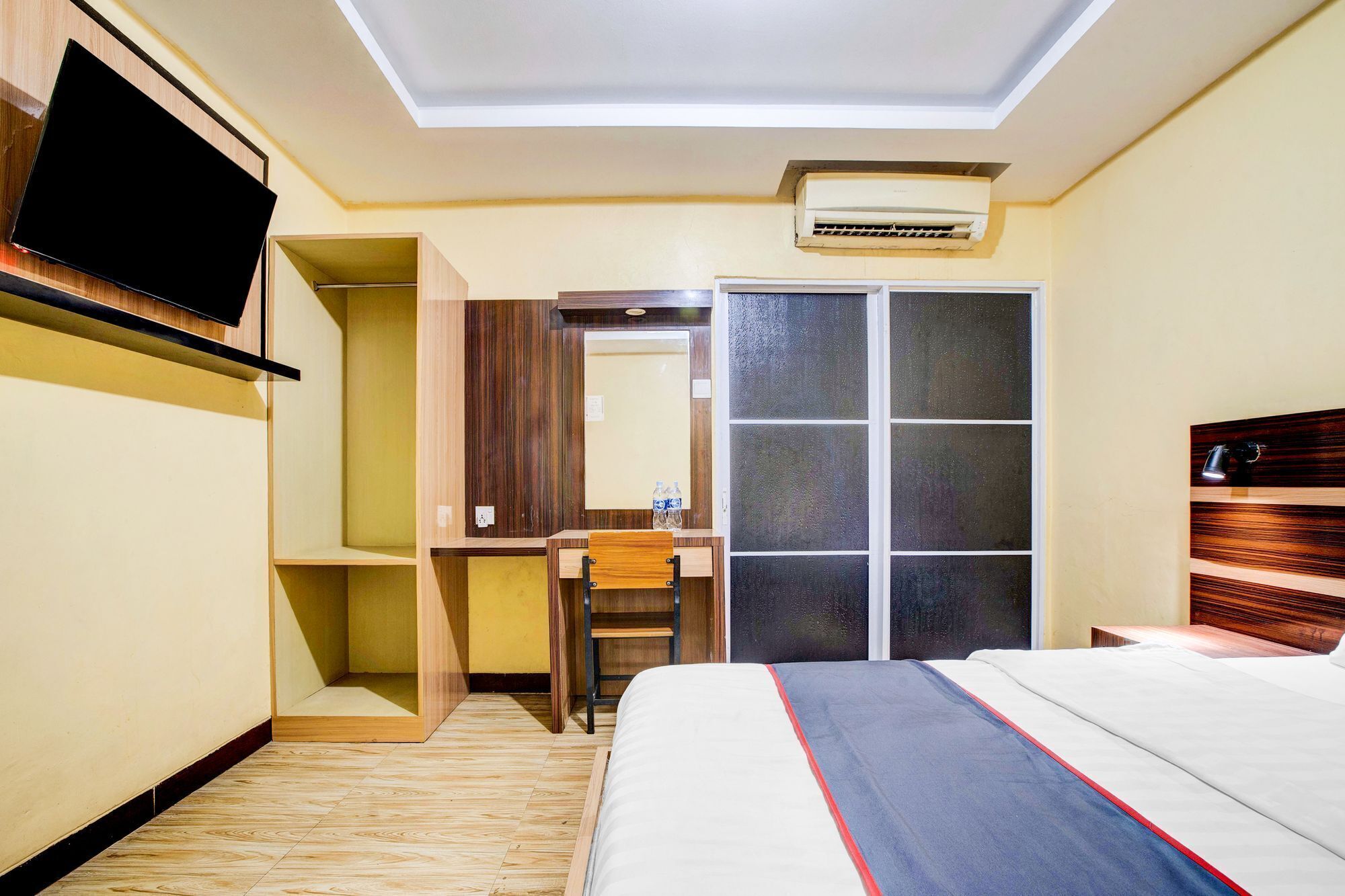 Quarto de hotel com cama, escrivaninha, cadeira, guarda-roupa e televisão.
