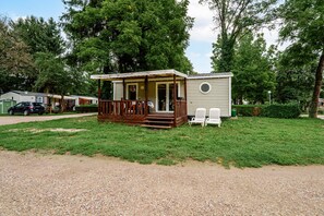 A small, single-story mobile home with a porch and a deck, surrounded by a grassy area and trees. - Apartment 'Lydia's Mobilhome' with Shared Pool, Private Terrace and Garden (Boofzheim)