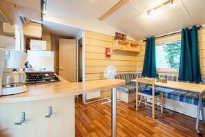 A compact kitchen with a stove, microwave, and sink. There is a dining area with a bench and a table.