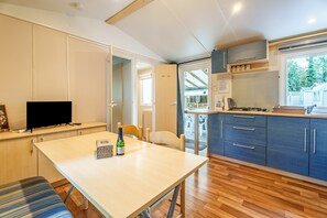 Une cuisine compacte avec un coin repas, une télévision et une bouteille de vin posée sur la table.