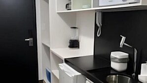A compact kitchen with white cabinetry, a microwave, a coffee machine, and a sink. - Flat 350m da praia de Tambaú - conforto (Joao Pessoa)