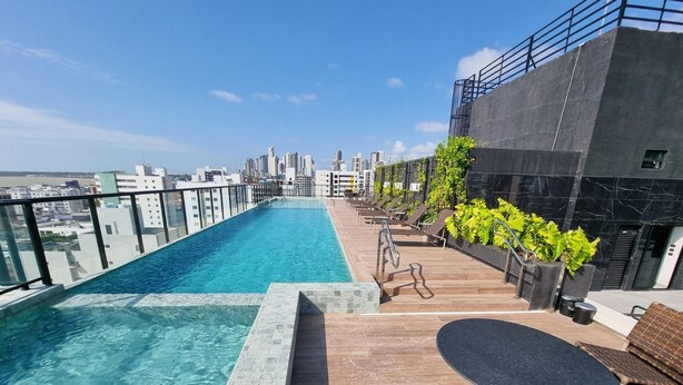 A rooftop infinity pool with a city view, lounge chairs, and a small table. - Flat 350m da praia de Tambaú - conforto (Joao Pessoa)