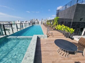 Evigheds-pool på taget med udsigt over byen, liggestole og et lille bord.