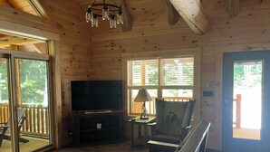 A cozy cabin interior with a large TV, wooden walls, a balcony, and a chair with a deer design. - "Hidden Pleasures" - "Hidden away in beautiful Hocking Hills" (Logan)