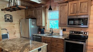 A cabin-style kitchen with wooden cabinets, a granite countertop, a refrigerator, a microwave, a stove, and a sink. - "Hidden Pleasures" - "Hidden away in beautiful Hocking Hills" (Logan)