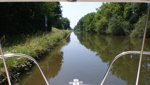 A narrow waterway flanked by dense greenery, viewed from a boat with metal railings. - Calm overnight aboard the JAVA boat, 30 minutes from PAL, disconnection guaranteed! (Luneau)