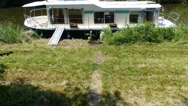 A houseboat with a covered deck, windows, and a flag. - Calm overnight aboard the JAVA boat, 30 minutes from PAL, disconnection guaranteed! (Luneau)