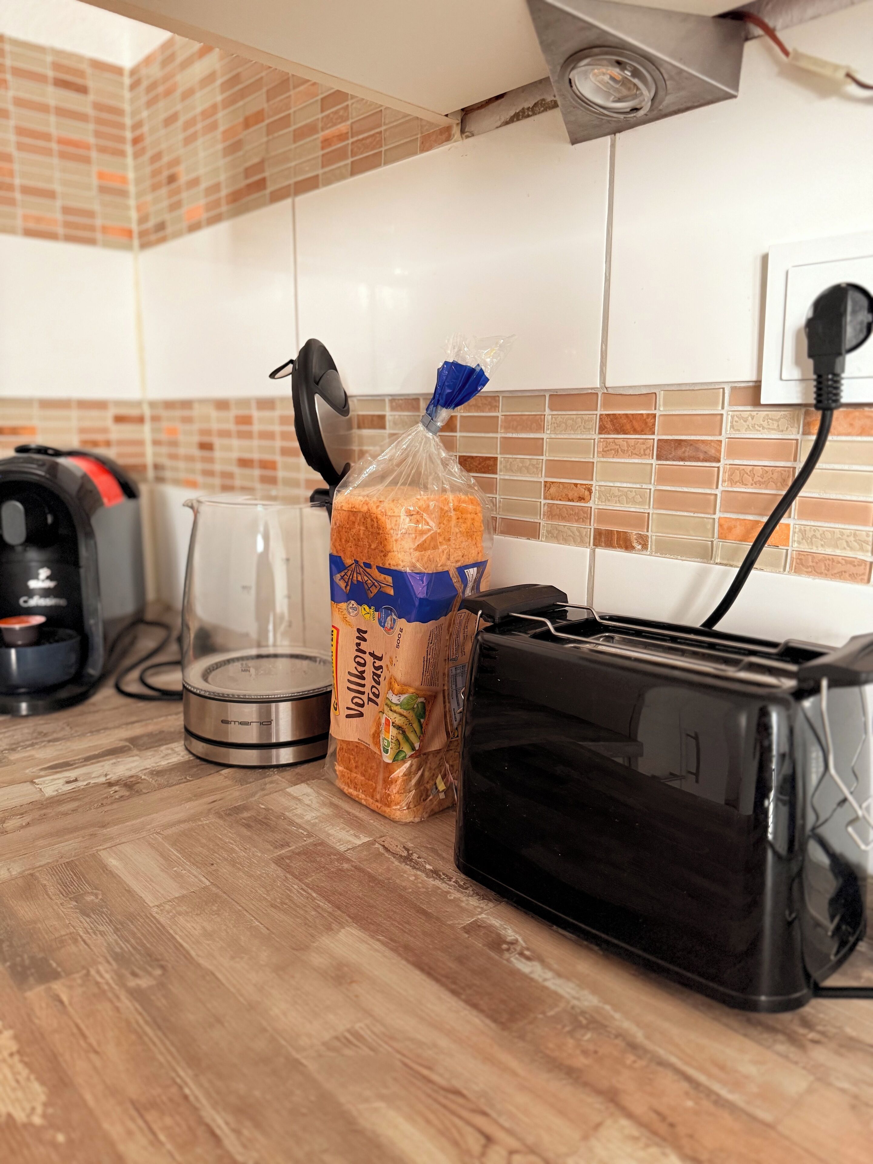 Una encimera de cocina con un tostador, una bolsa de pan, una tetera y una cafetera.