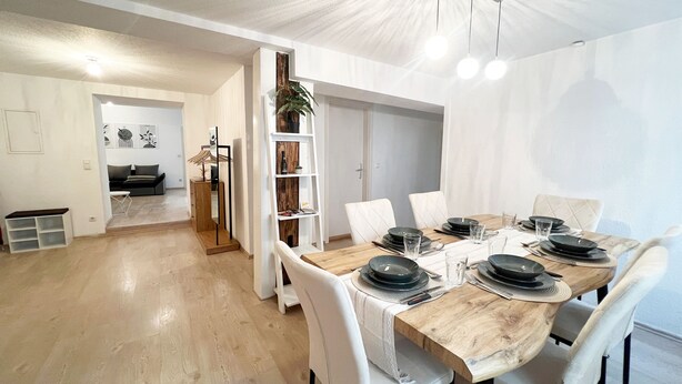 A dining area with a wooden table set for six, white chairs, and a modern interior design. - DREAMZzz AltstadtTraum in the heart of Coburg|Parking lot (Coburg)
