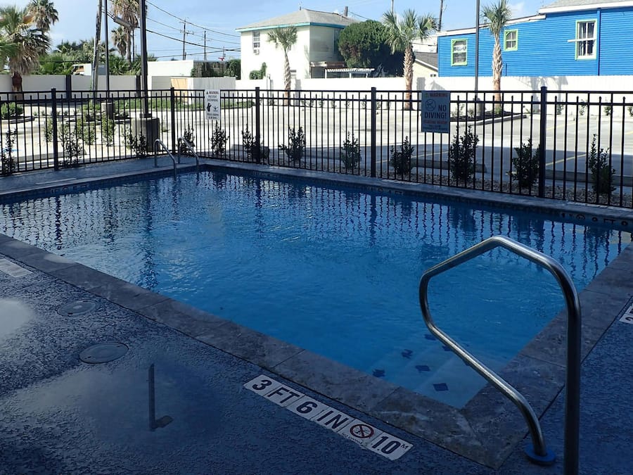 A swimming pool with a black metal fence, a lifeguard stand, and a sign indicating no diving.