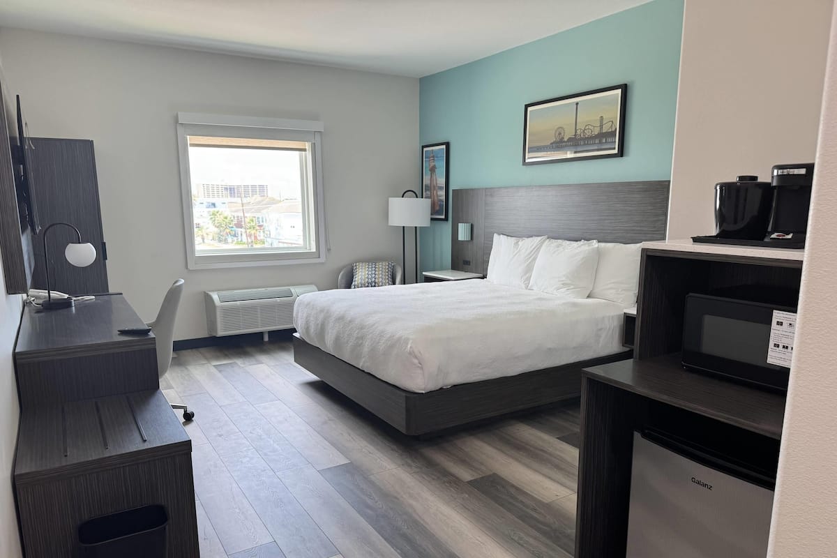 A modern hotel room with a bed, desk, chair, and a coffee machine.