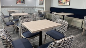 A modern dining area with striped upholstered chairs and light-colored tables, featuring artwork on the walls and a neutral color palette. - Seabreeze Hotel, An Ascend Collection Hotel (Galveston)