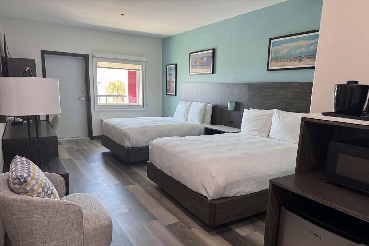A hotel room with two beds, a desk, a chair, and a window.