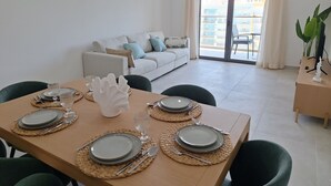 Ein Essbereich mit Tisch für vier Personen, einer Couch und Blick auf einen Balkon.