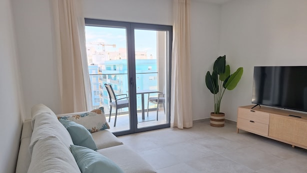Ein modernes Wohnzimmer mit einer Couch, einem Fernseher und einem Balkon mit Blick auf Gebäude.