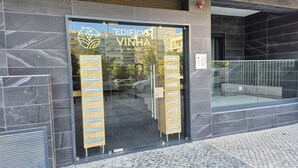 Der Eingang zu einem Gebäude mit einem Schild, auf dem 'EDIFÍCIO da VINHA' steht, und einer Glastür mit einem Zahlenschloss.