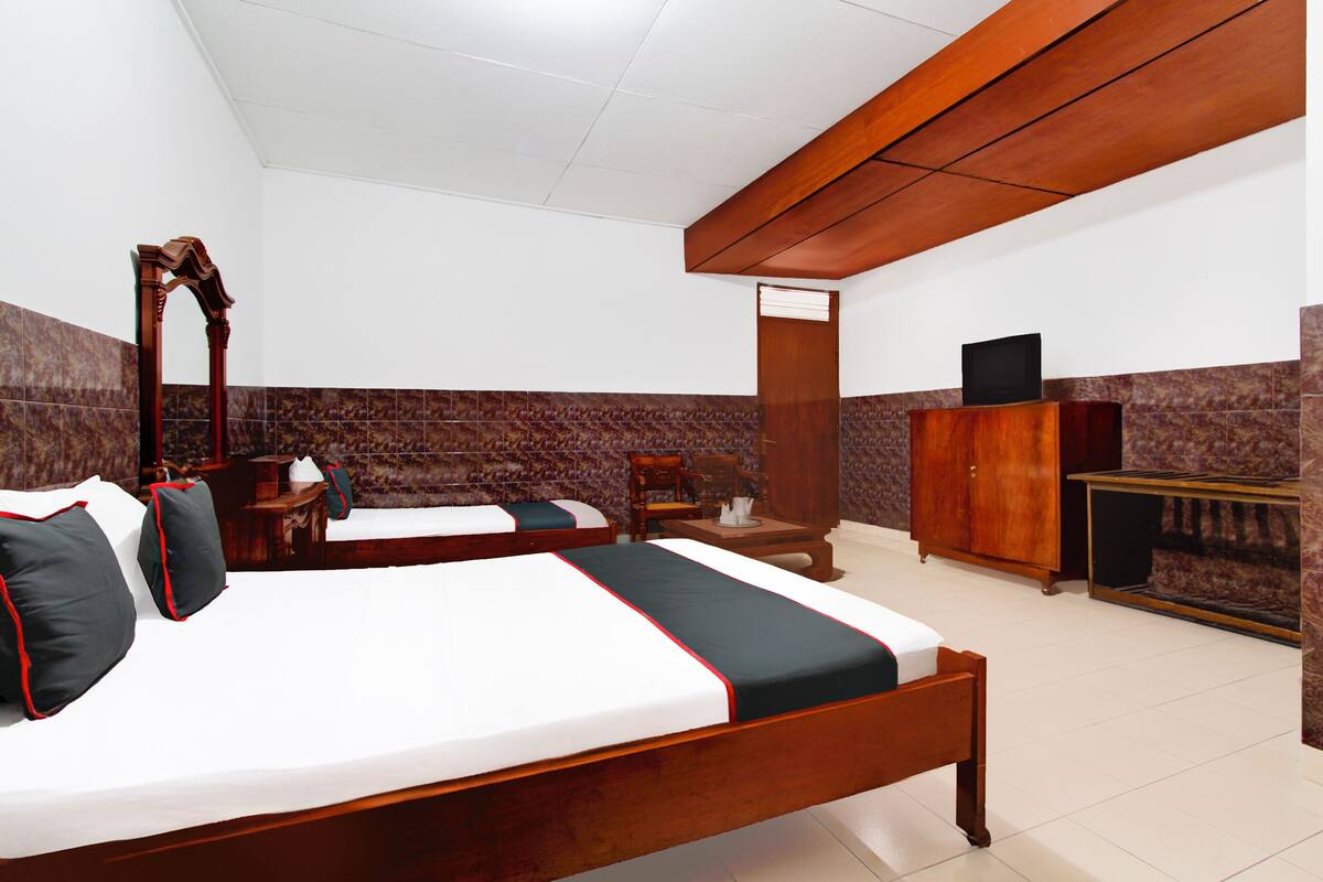 A hotel room with two single beds, a wooden wardrobe, a television on a stand, and a small table with a chair.