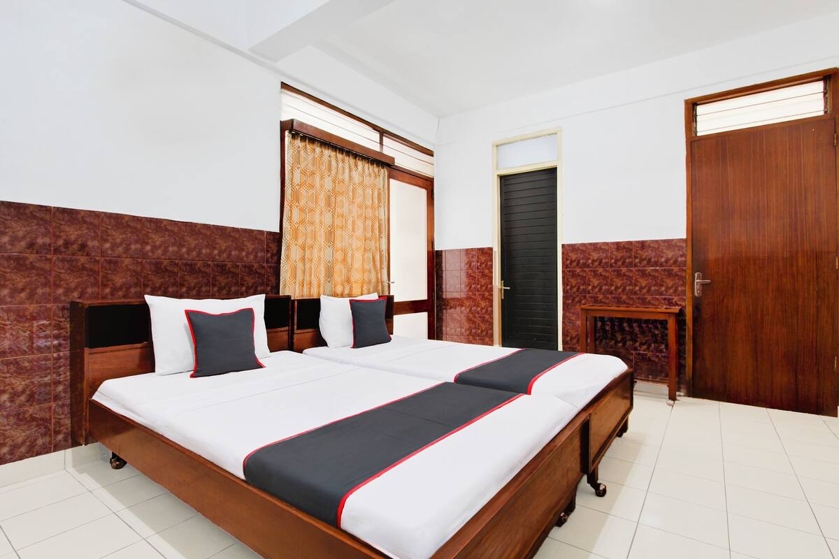 A double bed with a wooden frame, two bedside tables, a small wooden cabinet, and a door with a window.