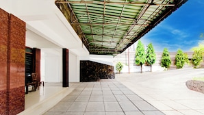 A covered outdoor area with a tiled floor, a stone wall, and a row of trees. - Hotel O Hotel Wisma Hasanah (Semarang)