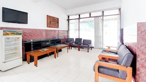 A spacious living area with a flat-screen TV, a refrigerator, a wooden coffee table, leather sofas, and a large window with blinds. - Hotel O Hotel Wisma Hasanah (Semarang)