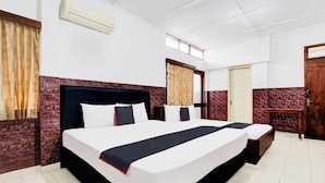 A hotel room with a large bed, a small bedside table, a wardrobe, and a window with curtains. - Hotel O Hotel Wisma Hasanah (Semarang)