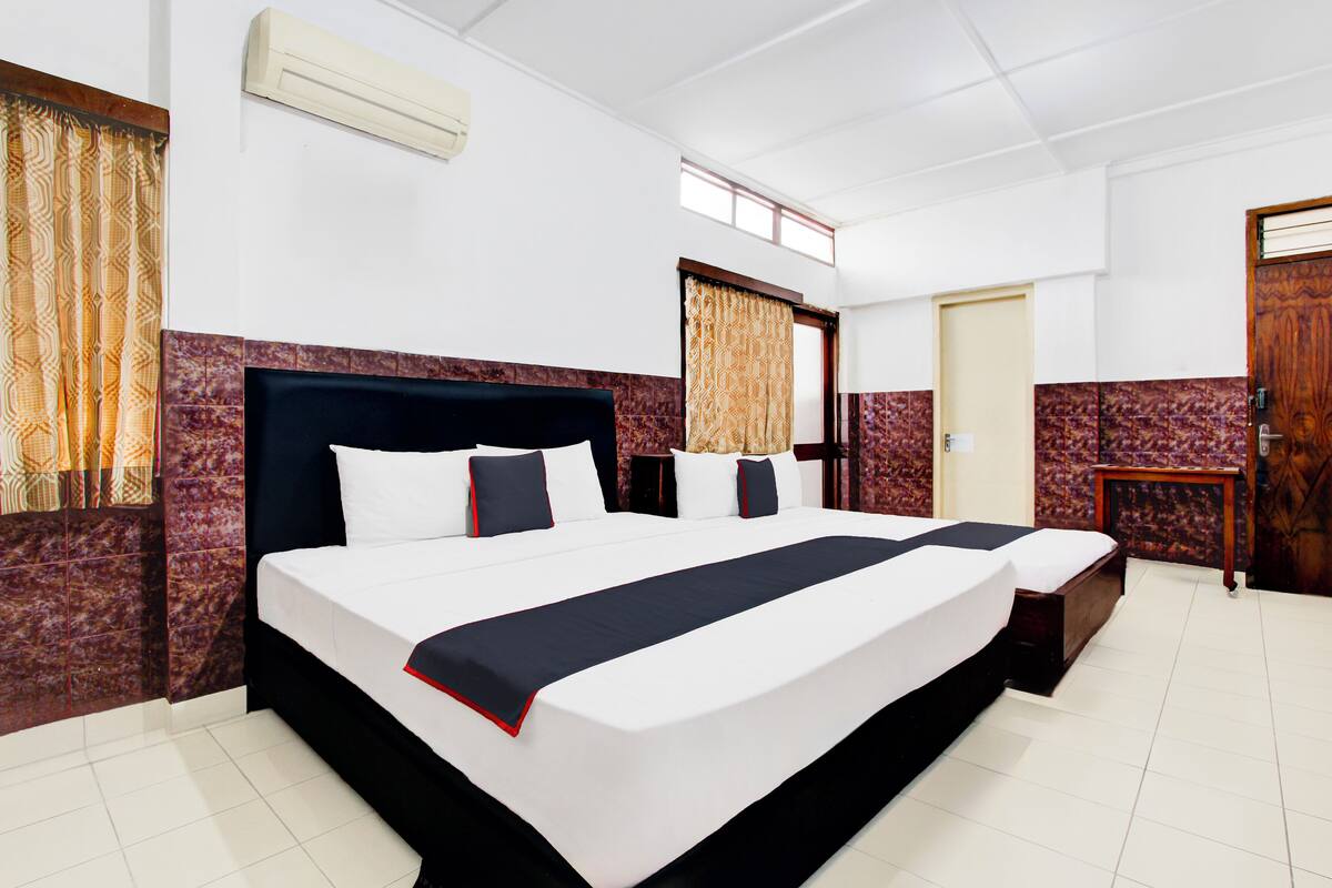 A hotel room with a large bed, a small bedside table, a wardrobe, and a window with curtains.
