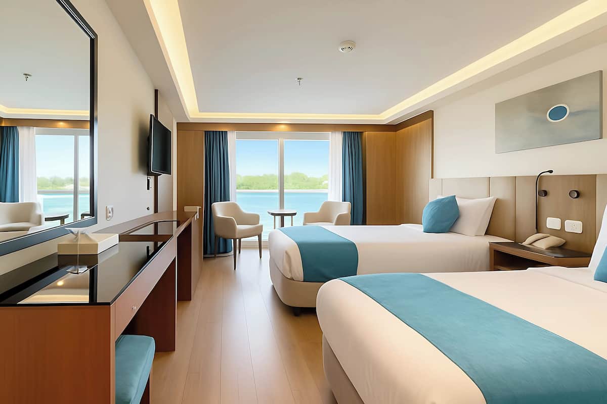 Ein Hotelzimmer mit zwei Betten, einem Fernseher, einem Schreibtisch und Meerblick.