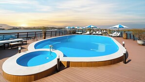 Ein Poolbereich mit Liegestühlen und Sonnenschirmen mit Blick auf ein Gewässer.