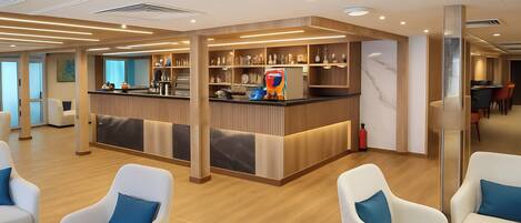 A modern hotel lobby with a reception desk, seating area, and a kitchen in the background.