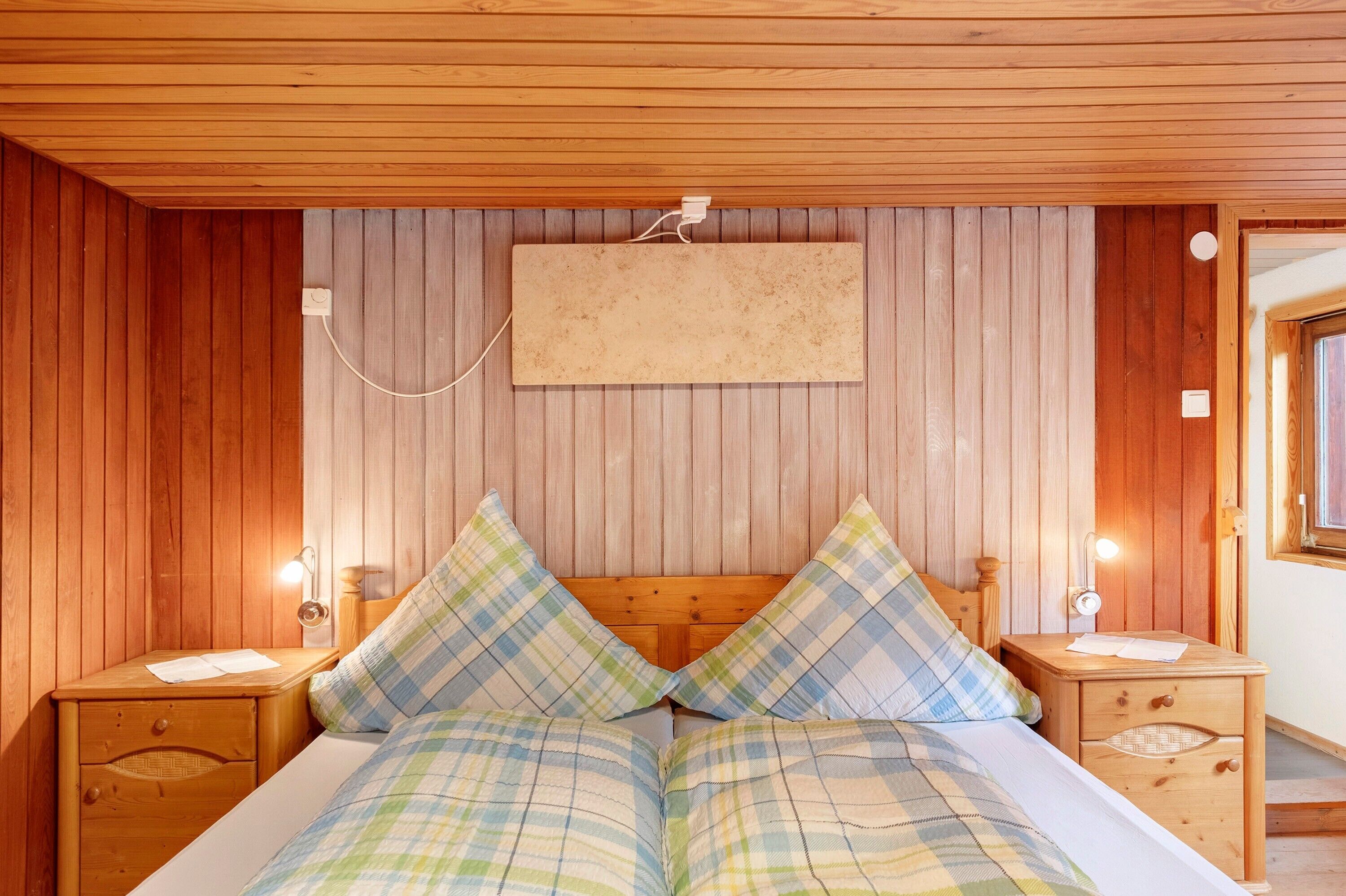 Habitación con paneles de madera, una cama, dos mesitas de noche y una lámpara fijada a la pared.