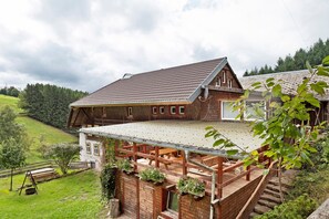 Una casa de madera con techo inclinado, un porche cubierto y vistas a un valle verde.