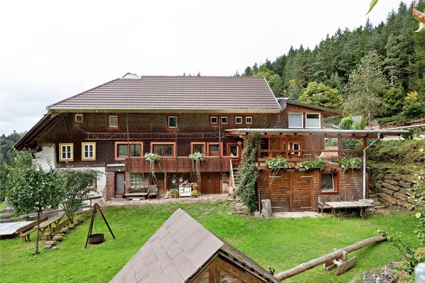 Una casa grande de madera con techo inclinado, un patio y vistas a una ladera boscosa.