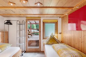 Una habitación de madera con literas, una escalera, un ventanal y una puerta que da a un espacio al aire libre.