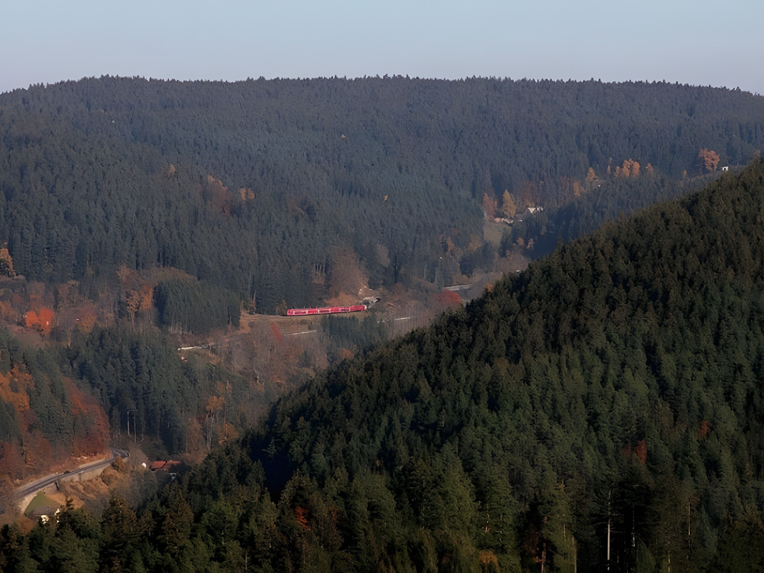 Un paysage montagneux, avec de vastes forêts et une voie ferrée.
