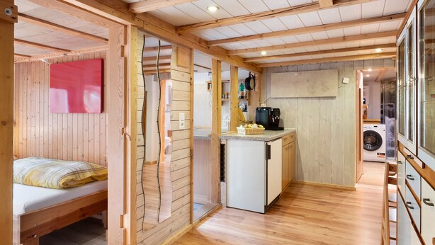 A compact room with a bed, a kitchenette, and a washing machine. - Apartment 'Schwäblehof' (Triberg im Schwarzwald)