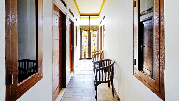 Un couloir avec des portes et des fenêtres en bois, un parquet à motifs en chevrons et une chaise placée au centre.