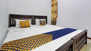 Un lit recouvert d’une couvre-lit à motifs, deux oreillers ornés de dessins géométriques et un mur décoré d’une tapisserie verticale à motifs.