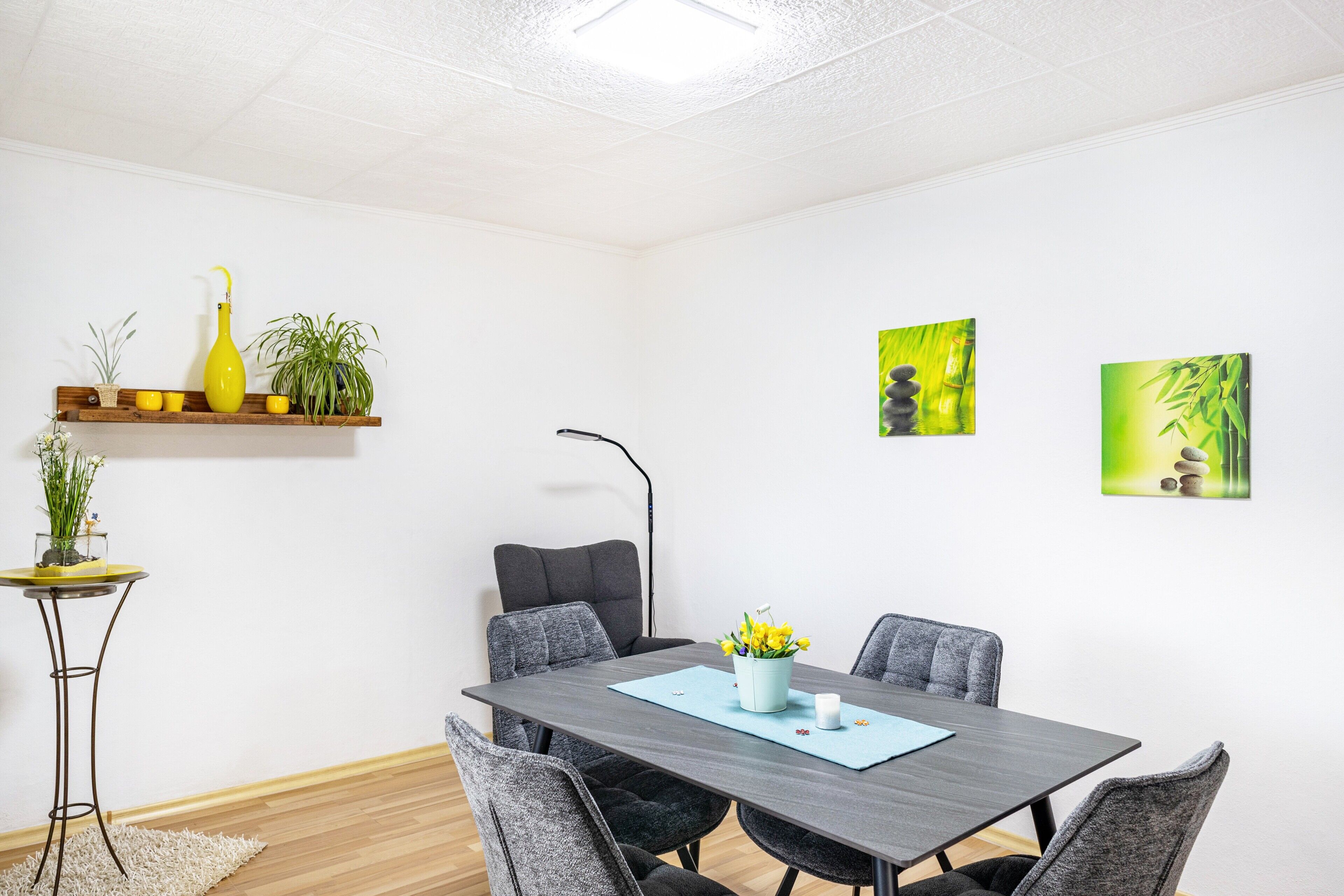 Uma sala de conferências com uma mesa de madeira escura, cadeiras estofadas em cinza, uma mesinha lateral com um vaso de planta e duas pinturas penduradas na parede.