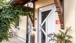 Entrada de un edificio con una pérgola de madera, un letrero de bienvenida, una puerta con panel de vidrio y una decoración navideña.