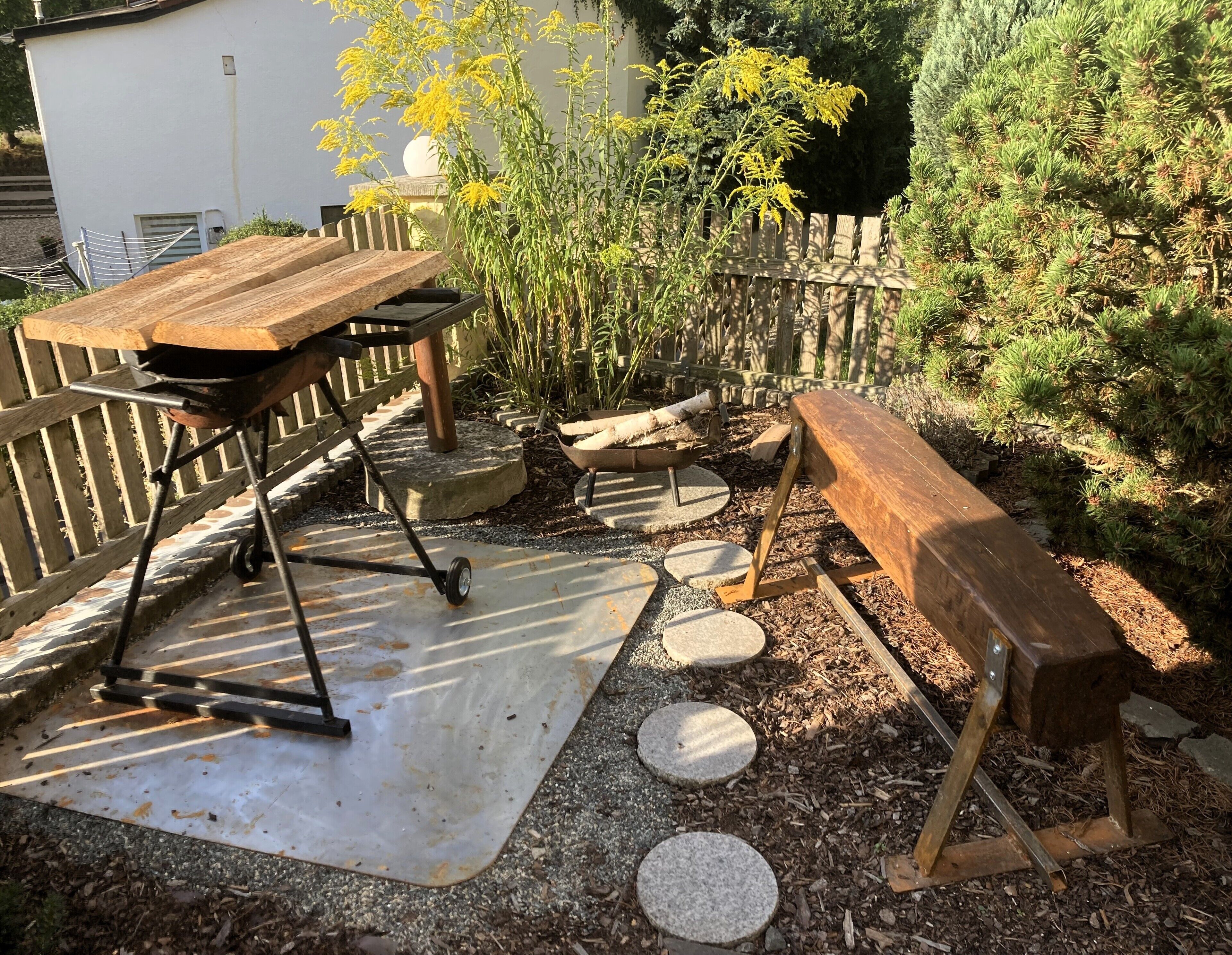 Een terras met een houten tafel, een barbecue, een kruiwagen en een bank.