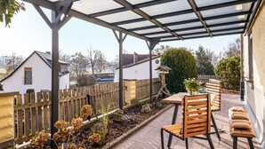 Un patio cubierto con una mesa y sillas, una valla de madera y un jardín con plantas.