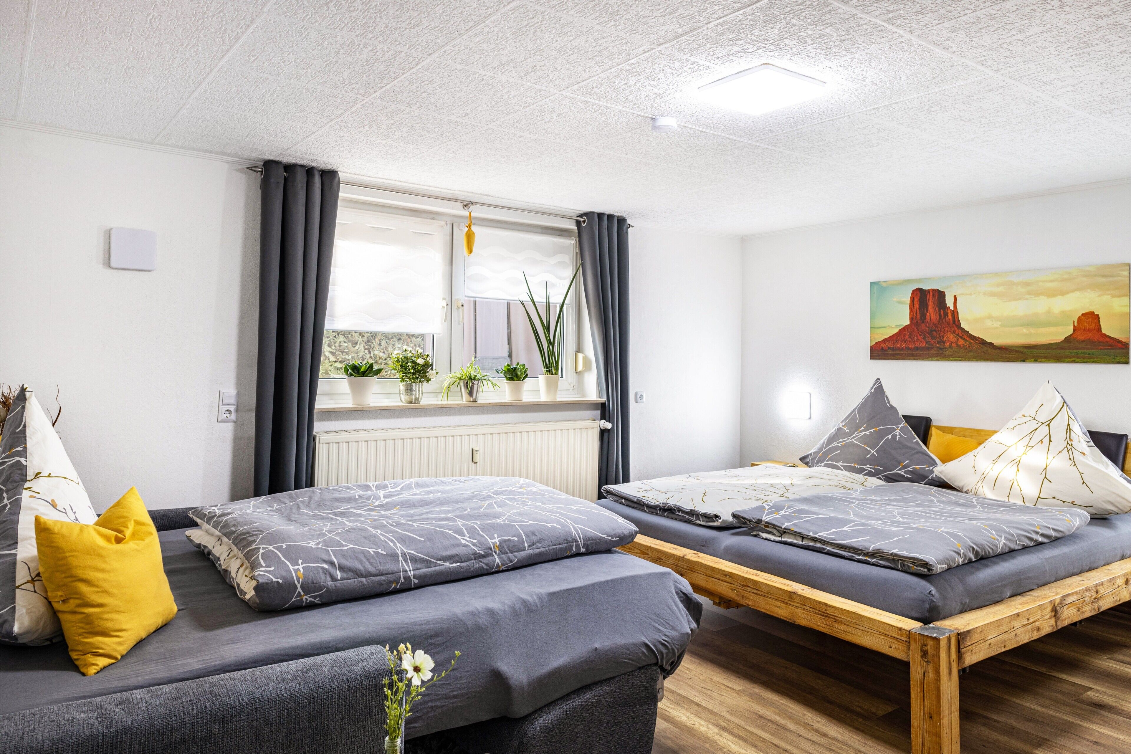 Una habitación de hotel moderna con dos camas, una ventana con cortinas, un radiador y un cuadro en la pared.
