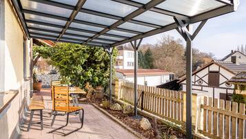A covered patio with a table and chairs, a wooden fence, and a house in the background.