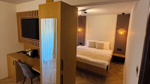 A modern hotel room with a wooden desk, a bed with white bedding, and a large window with curtains. - Pensiunea AN de AN (Remeţi)