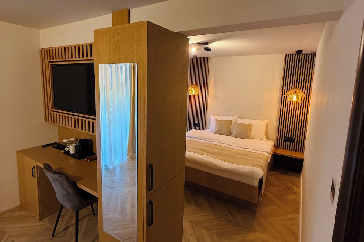 Une chambre d’hôtel moderne avec un bureau en bois, un lit avec une literie blanche et une grande fenêtre avec des rideaux.